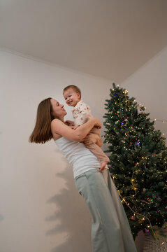 A mother and daughter celebrate the New Year under a Christmas tree with garlands and lights. A happy, emotional photo of real people, a homey atmosphere.