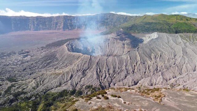 Aerial view from Mount Batok toward Mount Bromo, highlighting its intricate volcanic formations and the vast Tengger caldera rim in bright daytime light, Indonesia