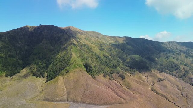 Drone flight over the Teletubby Hills near Mount Bromo, showing dry brown lower slopes contrasting with green hilltops during the dry season, Indonesia