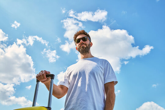 Low Angle View of Young Bearded Man with Suitcase Ready for Travel Against Blue Sky