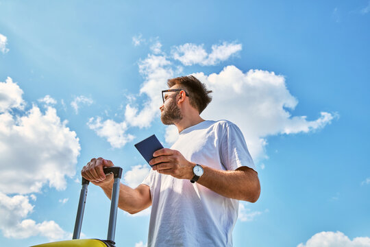 Low angle view of man with suitcase and passport looking at sky