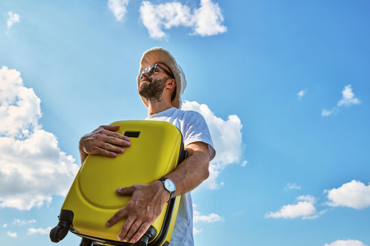Young Man Holding Yellow Suitcase Against Blue Sky Ready for Summer Vacation