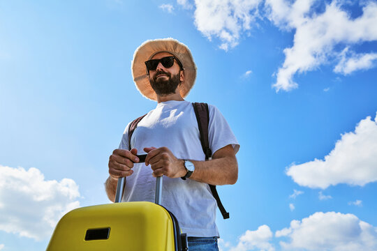 Low Angle View of Male Traveler with Yellow Suitcase Against Blue Sky