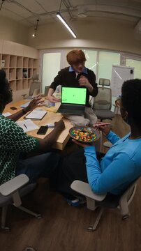 Vertical video of young adult Caucasian man presenting laptop with green screen to diverse African American colleagues. Clip is ideal for tech startup promos or software demo presentations