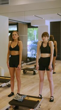 Two young women perform shoulder shrugs as part of their fitness workout in a modern gym. They are engaged in a healthy exercise routine at a Pilates studio.
