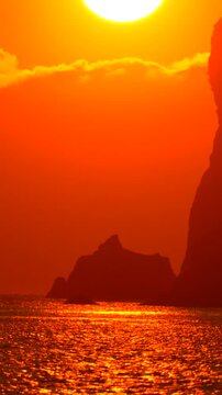 Sunset sea silhouette beautiful vertical sunset over the ocean with jagged rocks silhouetted against a fiery orange sky