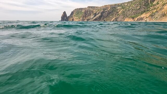 Ocean waves cliffs ripple on the emerald water surface while massive rocky headlands stand tall under a clear and bright summer sky