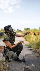 Fototapeta premium A resilient survivor wearing a gas mask crouches on a ruined road, searching for hope in a bleak, postapocalyptic wasteland. Evokes feelings of suspense, survival, and isolation.