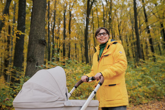 Young mother walking with baby stroller in autumn forest