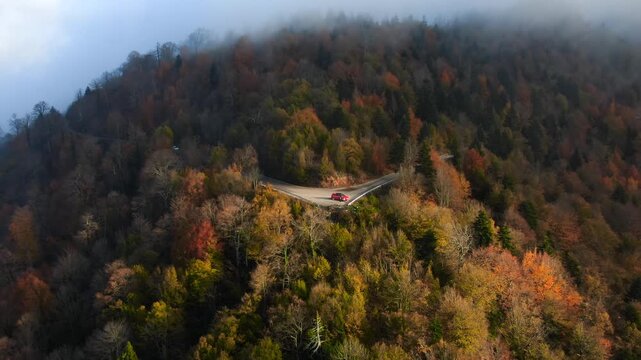 Drone pulling back from a tiny red car parked on a mountain hairpin turn to reveal misty peak and vast wilderness.