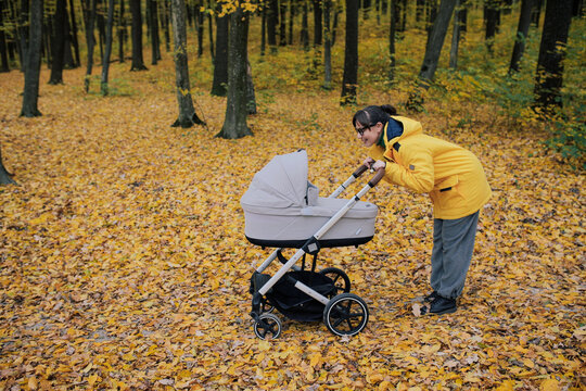 Young mother walking with baby stroller in autumn forest