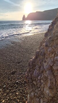 Seaside sunset landscape featuring gentle ocean waves crashing against a rugged pebble beach at Fiolent. Low angle tracking shot.