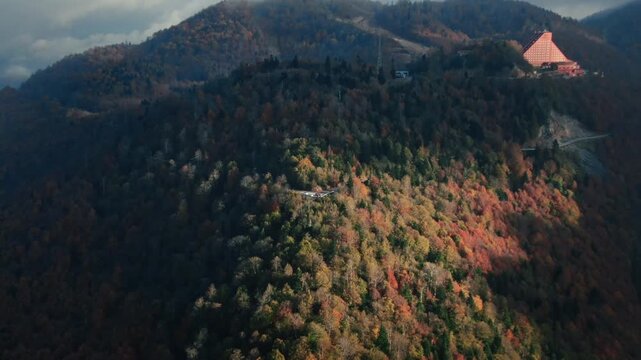 Panoramic aerial view of a ski resort hotel perched on mountain peak surrounded by autumn forest. Drone pulling back on Kartepe muntain hairpin turn to reveal misty peak and vast wilderness