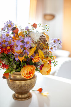 Floral arrangement in brass vase. Fall interior decor of living room. Home decorated for autumn with bouquet of rose aster flowers