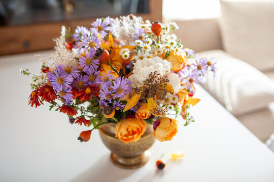 Floral arrangement in brass vase. Fall interior decor of living room. Home decorated for autumn with bouquet of rose aster flowers