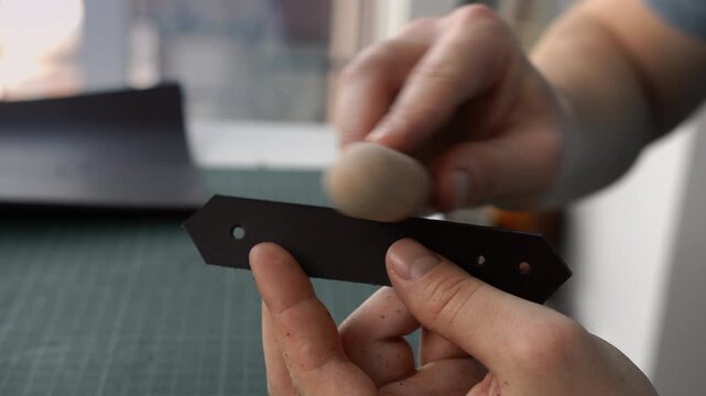 Craftsman burnishing the edge of a genuine leather strap with a wooden slicker in a workshop