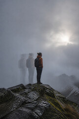 Naklejka premium Mountaineer stands resolute on a foggy ridge, surrounded by shifting silhouettes guiding the way forward