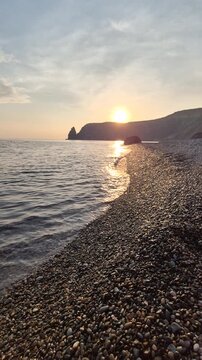 Golden sunset, rocky beach, and gentle waves wash onto the shore at Fiolent Cape. Stationary wide angle shot.