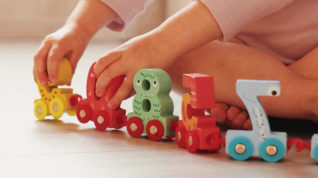 Close-up of hands moving a colorful toy train with numbered pieces during playful learning.