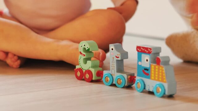 Mother and child hands interact with a colorful numbered toy train during playful learning at home.