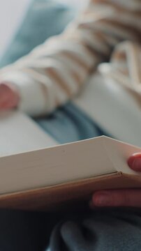 Vertical video. Woman reading book, close-up, in cozy home setting. Embracing leisure and love for reading.