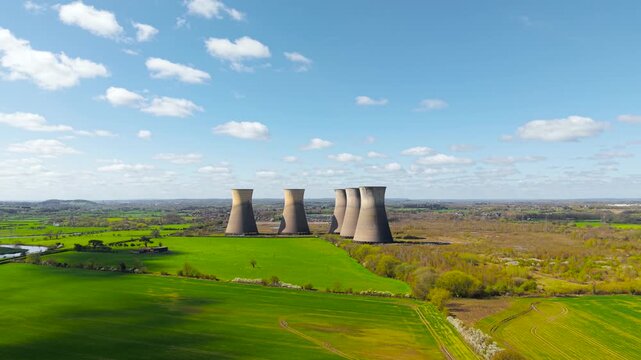 Abandoned nuclear cooling towers in wide countryside landscape under blue sky industrial decline and environmental recovery concept. Green farmland surrounding empty facility highlighting nature