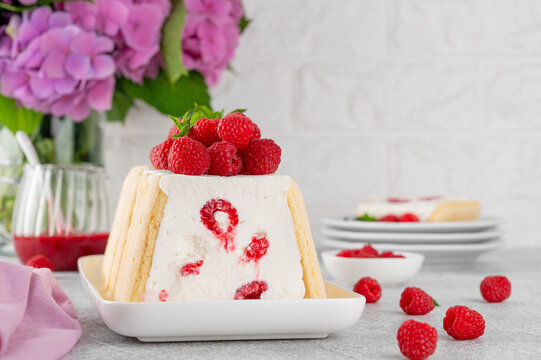 No baked cheesecake or mousse cake with raspberries and savoiardi (lady fingers) cookies on a white plate on a stone background. Copy space.
