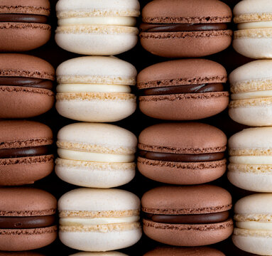 White and dark French macarons with chocolate ganache filling on a brown paper background. Modern minimalism concept. Close up, top view, copy space.