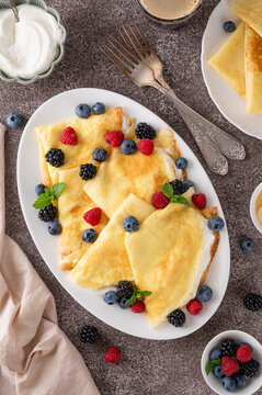 Crepes or thin pancakes with cream cheese, fresh berries and honey on a white plate on a concrete background. Copy space
