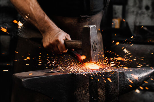 A blacksmith is hammering glowing hot metal on an anvil, creating sparks in a dark workshop setting.