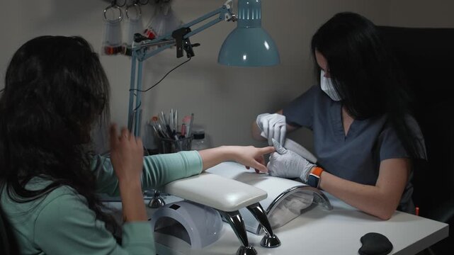 Manicure technician corrects nail shape with file in beauty salon during professional hand care process