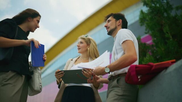 Business people engage in an outdoor discussion while reviewing documents. A professional team collaborates on a project outside the office.