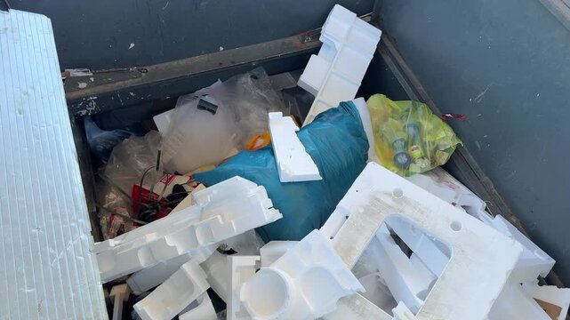 Plastic and polystyrene waste being thrown into a large collection container at a recycling center