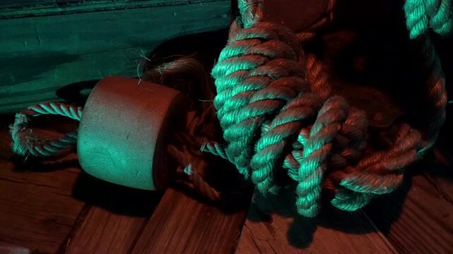 Coiled rope and a cork buoy lay on a wooden deck lit by torchlight.