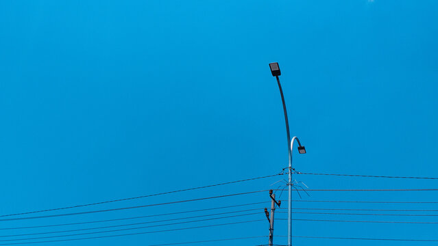 Minimalist street light pole with electric utility wires under a clear vibrant blue sky background, urban outdoor infrastructure design