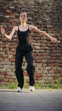Young professional Hispanic dancer performing salsa in front of a brick wall while recording a video for social media, capturing urban dance culture, energy and modern content creation.