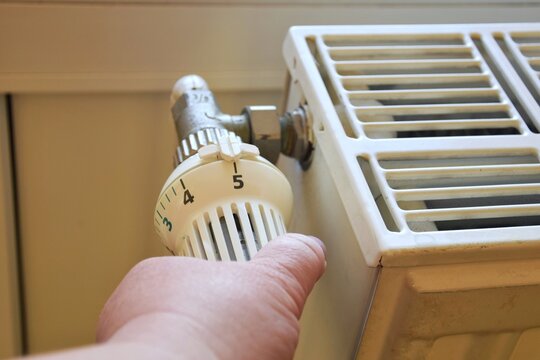 A woman turns on a radiator to create a comfortable atmosphere in the house during the cold season. A woman adjusts the temperature on a radiator. Heating, rising utility costs.