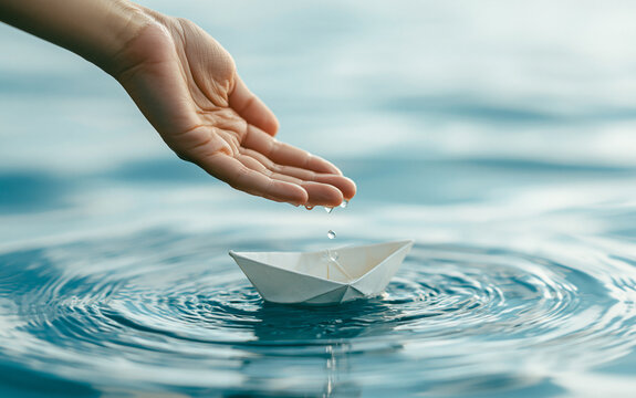 Hand reaching for white paper boat floating on blue sea water