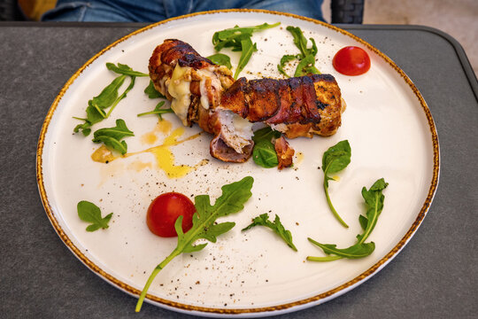 Pork roulade with cheese, herb leaf, oil and cherry tomato on big plate.