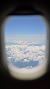 Stunning aerial view of fluffy white clouds and blue sky seen through airplane window during flight.