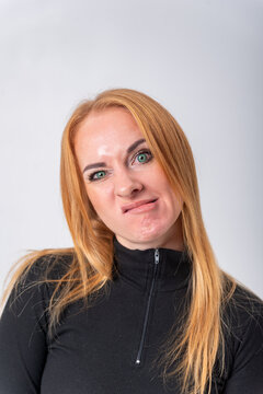Young woman posing with a displeased facial expression, scrunching her nose and pursing her lips, communicating disapproval or distaste on a light background