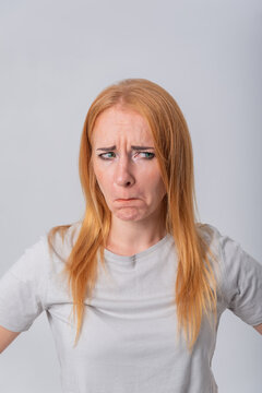 Young redhead woman with furrowed brow and pouting lips looks away in skepticism and annoyance, conveying doubt, disappointment and thoughtful displeasure against a plain studio background