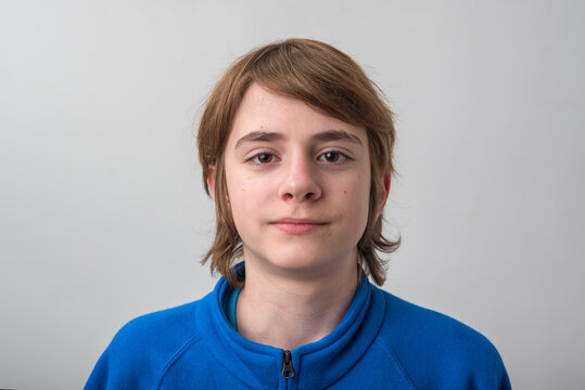Adolescent with brown hair and serious look, wearing a blue sweatshirt, standing against a plain white background, conveying youth, identity, and individuality