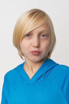 Blonde haired child posing in a blue hooded sweatshirt, making a silly expression with puckered lips and looking directly at the viewer on a white background