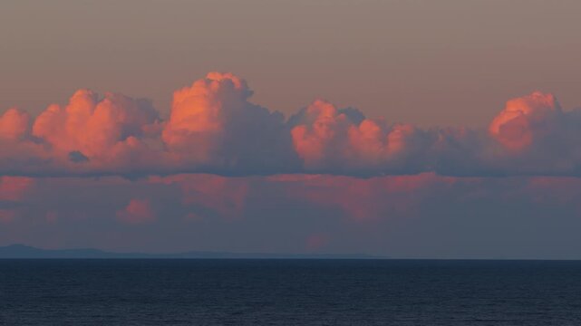 Dramatic time-lapse of orange and pink clouds rolling over vast ocean at sunset or sunrise.