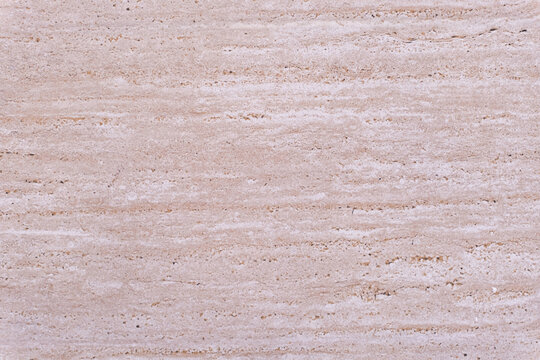 Natural travertine stone surface displaying a warm beige and pinkish hue. Featuring distinct horizontal striations and a porous