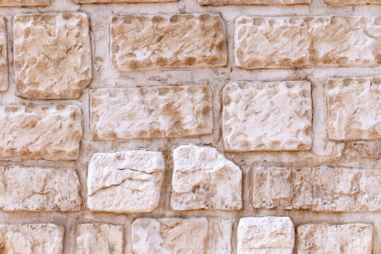 Natural stone wall displaying rough, light colored, irregularly shaped blocks cemented together, forming an organic and weathered background texture