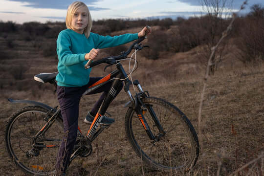 Young boy with blond hair posing with his mountain bike on a dry grassy hill, looking at the camera, conveying childhood adventure and freedom in an outdoor landscape