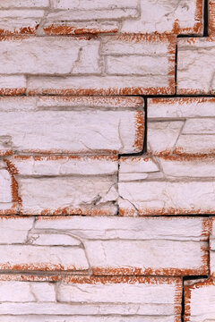 Rough white stone wall surface showing an interlocking block pattern with rustic reddish orange edges, creating a weathered and abstract textured background