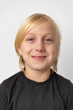 Blond young boy with a cheerful facial expression is smiling confidently at the camera, portraying feelings of joy, childhood, and positive optimism